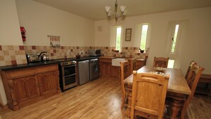 A spacious kitchen with wooden cabinets, a dining table, and chairs. - Lambley Farm-Orchard House (Lambley near Haltwhistle)
