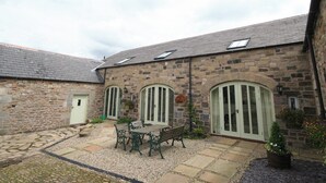 A stone building with a courtyard, featuring a table and benches, and a small garden area. - Lambley Farm-Orchard House (Lambley near Haltwhistle)