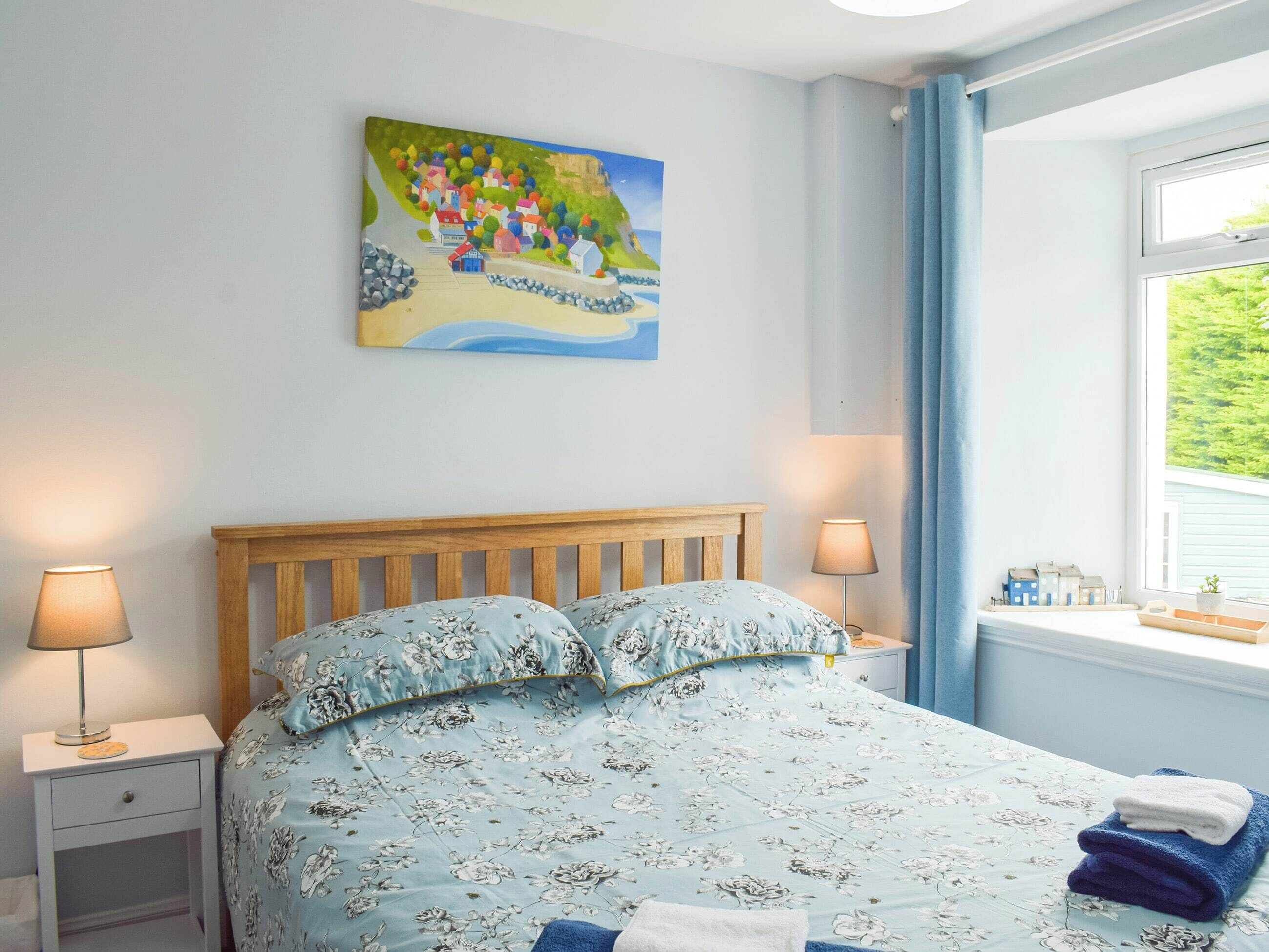 Une chambre à coucher comprenant un lit, deux tables de chevet, une commode, une fenêtre avec des rideaux et un tableau accroché au mur.