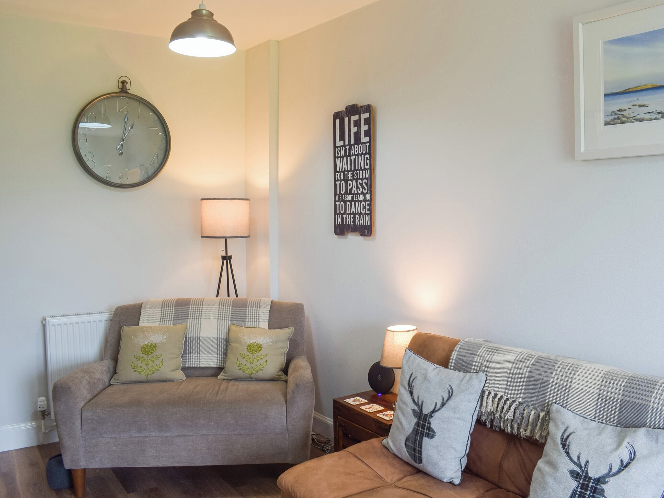 A living room with a grey sofa, a brown sofa, a round wall clock, a floor lamp, and a framed inspirational quote on the wall.