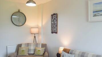 A living room with a grey sofa, a brown sofa, a round wall clock, a floor lamp, and a framed inspirational quote on the wall.