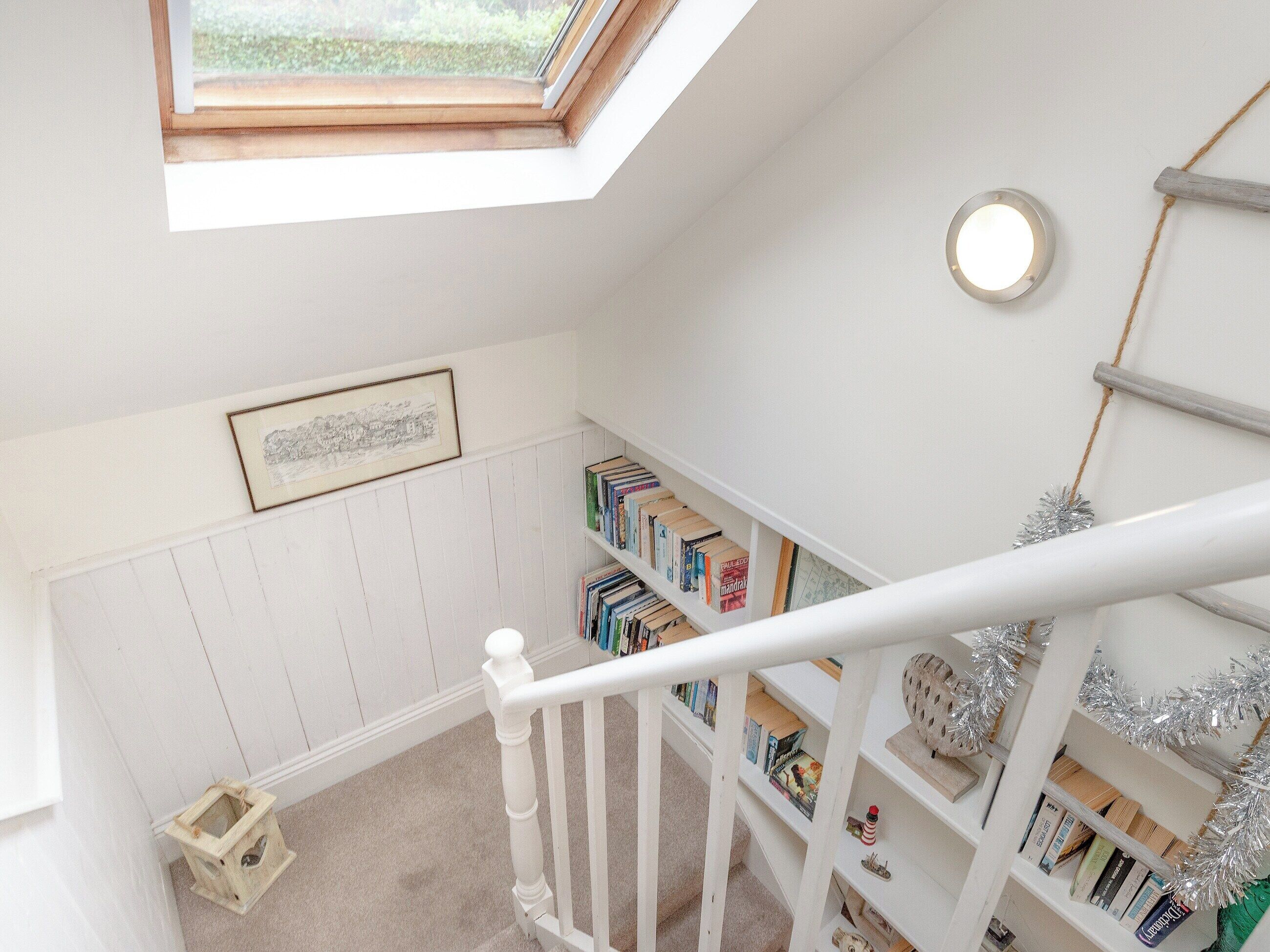 A room with a skylight, a bookshelf, a framed picture, and a small wooden stool.