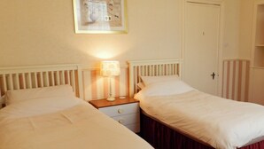 Habitación doble con dos camas, una mesita de noche con lámpara, una puerta y una cortina a rayas.