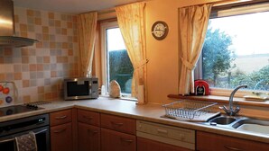 Una cocina con microondas, pileta y ventana con cortinas.