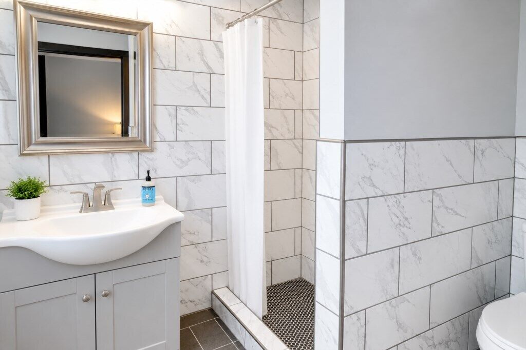 Un baño con lavamanos blanco, espejo, ducha e inodoro.