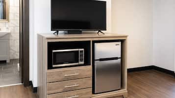 Une cuisine compacte équipée d’un four à micro-ondes encastré, d’un réfrigérateur en acier inoxydable et d’un téléviseur à écran plat posé sur un meuble en bois.