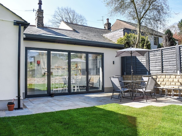 A modern house with a glass conservatory, a patio with outdoor furniture, and a stone wall.