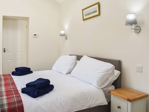 A neatly made bed with white linens and blue towels, a bedside table with a lamp, and a door in the background.