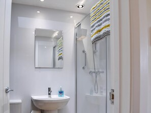 A modern bathroom with a glass shower enclosure, a white sink with a mirror above it, and a towel rack with a striped towel.