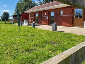 A red building with a covered patio, a trash bin, and a grassy area.