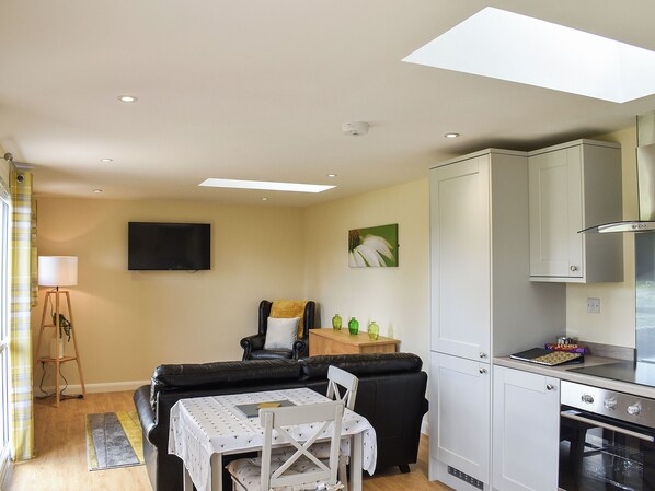 A compact living space with a sofa, dining table, kitchen area, and a flat-screen TV mounted on the wall.