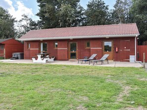 Un bâtiment rouge avec un toit en tuiles, une porte d’entrée et un petit porche agrémenté de deux chaises et d’une table.