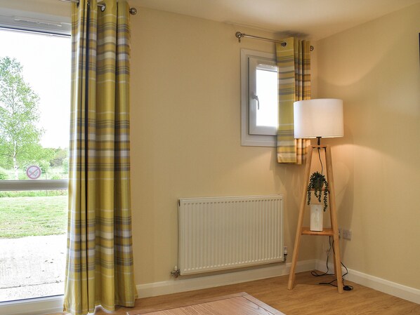 A room with a window, a radiator, a lamp on a wooden stand, and a view of greenery outside.