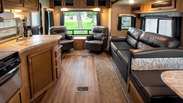 An RV interior with a kitchen, seating area, and a view of the outside.