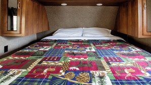 A bed with a colorful quilt, wooden cabinets above, and a carpeted floor.