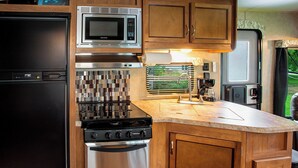 A compact kitchen with a refrigerator, microwave, stove, oven, and wooden cabinets.