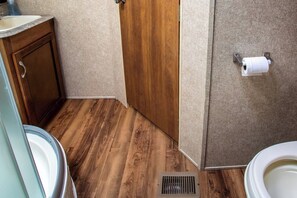 A bathroom with wooden flooring, a toilet, a sink, and a shower.