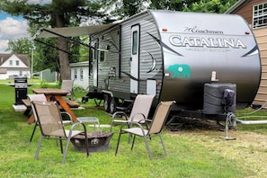 Una caravana Coachmen Catalina Legacy Edition con un porche cubierto, una parrilla y un tanque de agua.