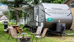 A recreational vehicle with a grill, a table, and chairs set up in a grassy area.