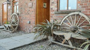 A brick building with a wooden door, two windows, and a large wooden wheel. - Mulberry Cottage - CC253015 (Skerne, near Driffield)