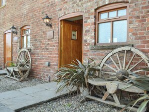 A brick building with a wooden door, two windows, and a large wooden wheel.