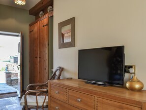 A wooden cabinet with a flat-screen TV, a wicker chair, and a small table with a vase.