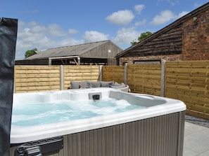 Een jacuzzi in een achtertuin met een houten omheining, een bakstenen muur en een houten gebouw op de achtergrond.