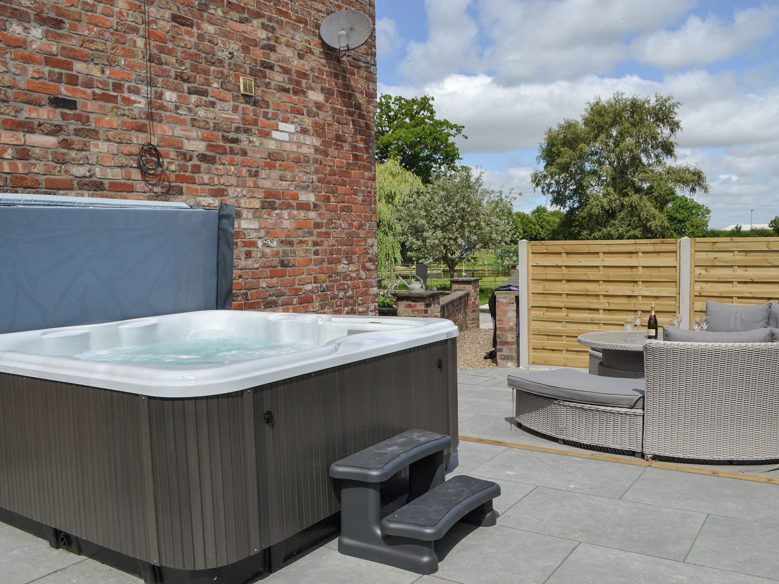 A hot tub with steps, a brick wall, and a wooden fence in a backyard setting.