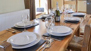 A dining table set with plates, glasses, and cutlery, a bottle of Prosecco, and a window with curtains. - Mulberry Cottage - CC253015 (Skerne, near Driffield)