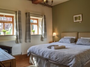 A bedroom with a bed, a nightstand, a lamp, a window with curtains, and a radiator. - Mulberry Cottage - CC253015 (Skerne, near Driffield)