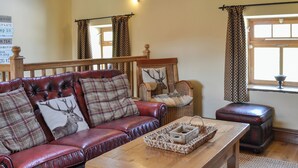 A cozy living room with a red leather sofa, a wooden coffee table, and a wicker basket. - Mulberry Cottage - CC253015 (Skerne, near Driffield)