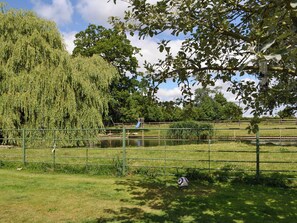 Een omheind park met een vijver, bomen en een speeltuin.