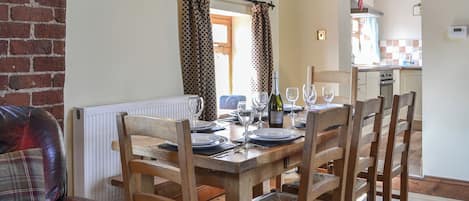 Un comedor con una mesa de madera dispuesta para cuatro personas, rodeada de sillas de madera. Se ve un sofá de cuero rojo al frente.