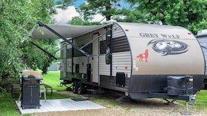 Una caravana Grey Wolf con un porche cubierto, una parrilla y una mesa de picnic.