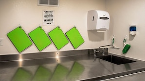 Un lavamanos de acero inoxidable con un dispensador de jabón, un cubo de basura y etiquetas verdes en la pared.