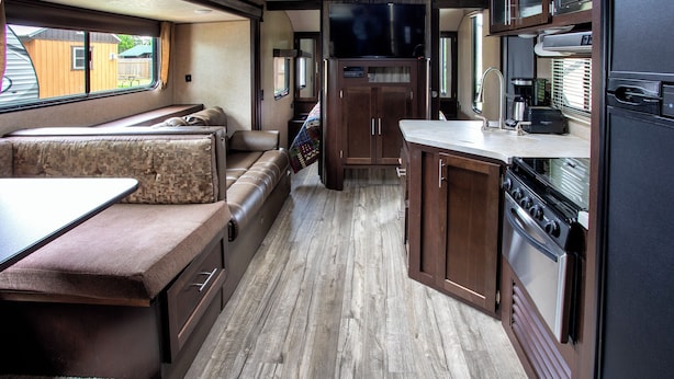 Una cocina compacta para autocaravana con armarios de madera, estufa y zona de comedor con banco.