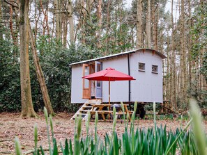 A small wooden cabin with a red umbrella, surrounded by trees. - Goosewing Hut-QU7072 (Melton Constable)