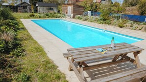 Una piscina rectangular con cubierta de madera y una mesa de picnic con un libro y un vaso.