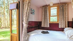 Un dormitorio con cama de madera, ventana con cortinas, puerta que da al exterior y un cuadro en la pared.