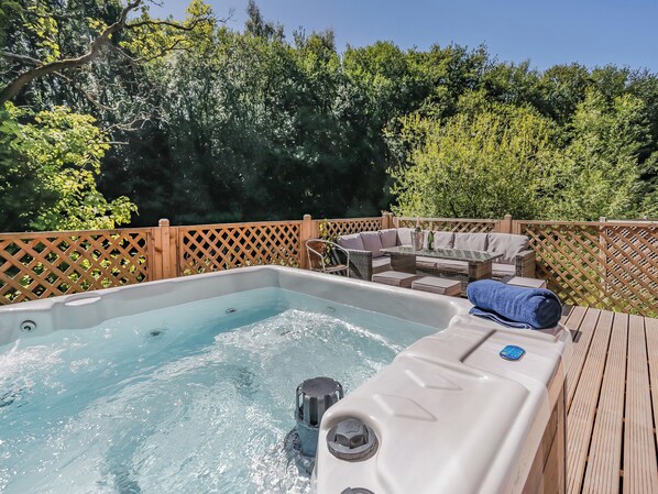 Un jacuzzi con panel de control, rodeado por una terraza de madera y una zona de estar con cojines.