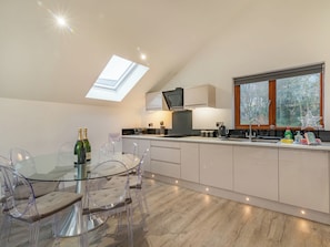 A modern kitchen with a glass dining table, clear chairs, a built-in oven, and a window with a view of trees.