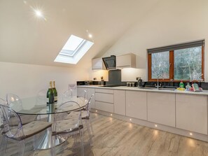 A modern kitchen with a glass dining table, clear chairs, a built-in oven, and a window with a view of trees.