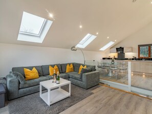 A modern living room with a sectional sofa, a glass coffee table, and a kitchen area with a glass dining table.