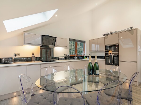 A modern kitchen with a glass dining table, clear chairs, and a built-in oven.