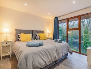 Un dormitorio moderno con una cama grande, dos mesitas de noche y vistas a zonas verdes a través de una ventana.