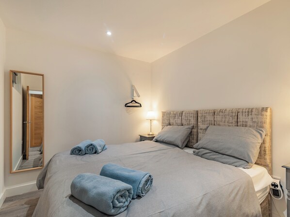 A bedroom with a bed, a bedside table with a lamp, a hanging clothes rack, and a mirror.