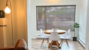 A modern dining area with a round wooden table, white chairs, and a potted plant. - Surf Shack- North Muskegon Oasis (Muskegon)