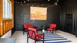 A room with a black brick wall, two red chairs, a blue and white striped rug, and a sunset painting. - Surf Shack- North Muskegon Oasis (Muskegon)
