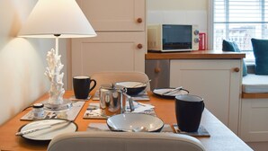 Een eethoek met een tafel gedekt voor twee personen, een lamp, een magnetron en een raam met zonwering.