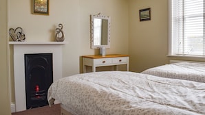 Een slaapkamer met twee bedden, een openhaard, een spiegel en een raam met jaloezieën.
